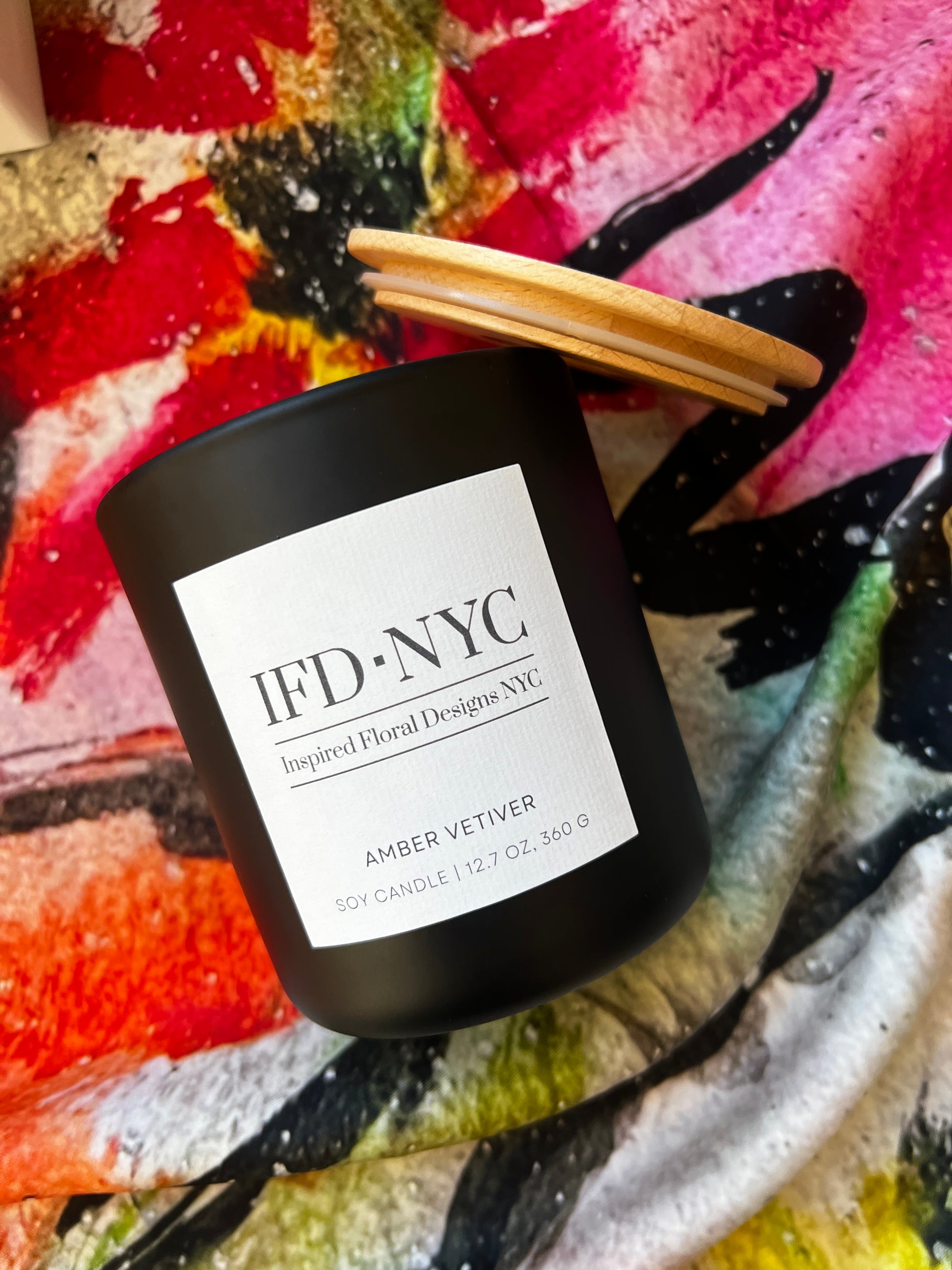 the inspired luxury candle amber vetiver Black candle with a wooden lid on a colorful abstract background