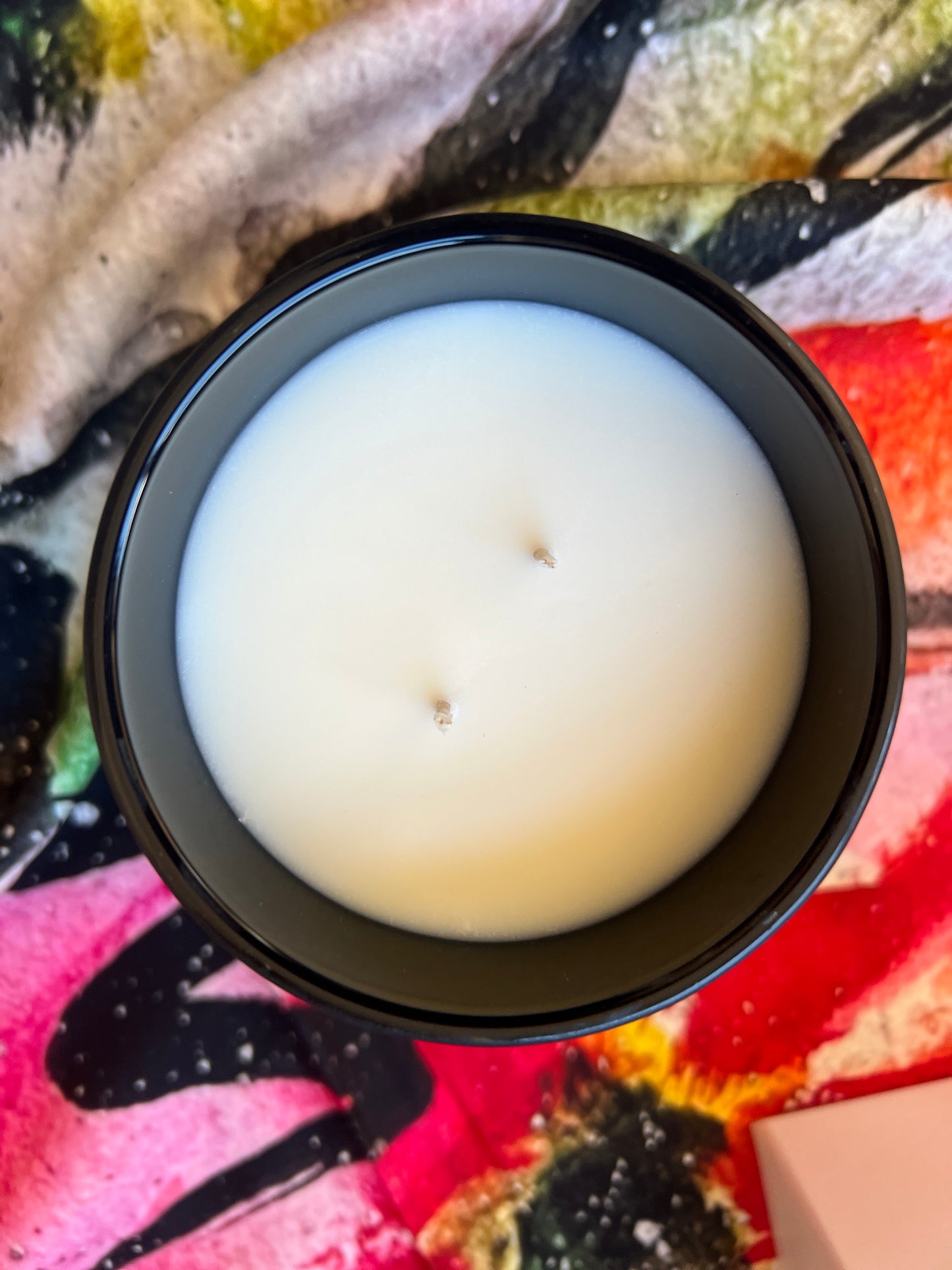 the inspired candle double wick White candle in a black container on a colorful fabric background