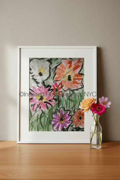 A framed floral art print by Barbara at Inspired Floral Designs NYC leaning against a beige wall on a wooden surface, with a small glass vase of flowers beside it. The artwork shows colorful flowers in pink, orange, purple, white, and green. Copyright