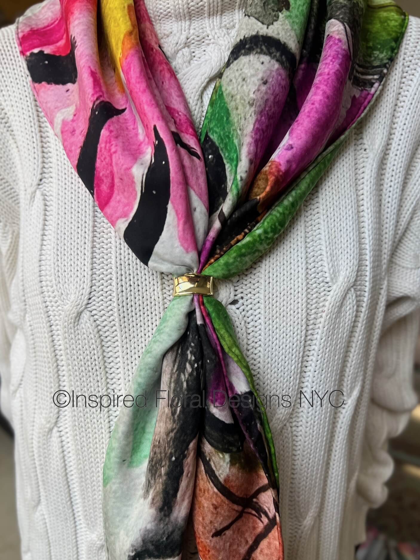Colorful floral-patterned scarf with a gold clasp on a white sweater, branded Inspired Floral Designs NYC copyright peace scarf the edit floral art in silk