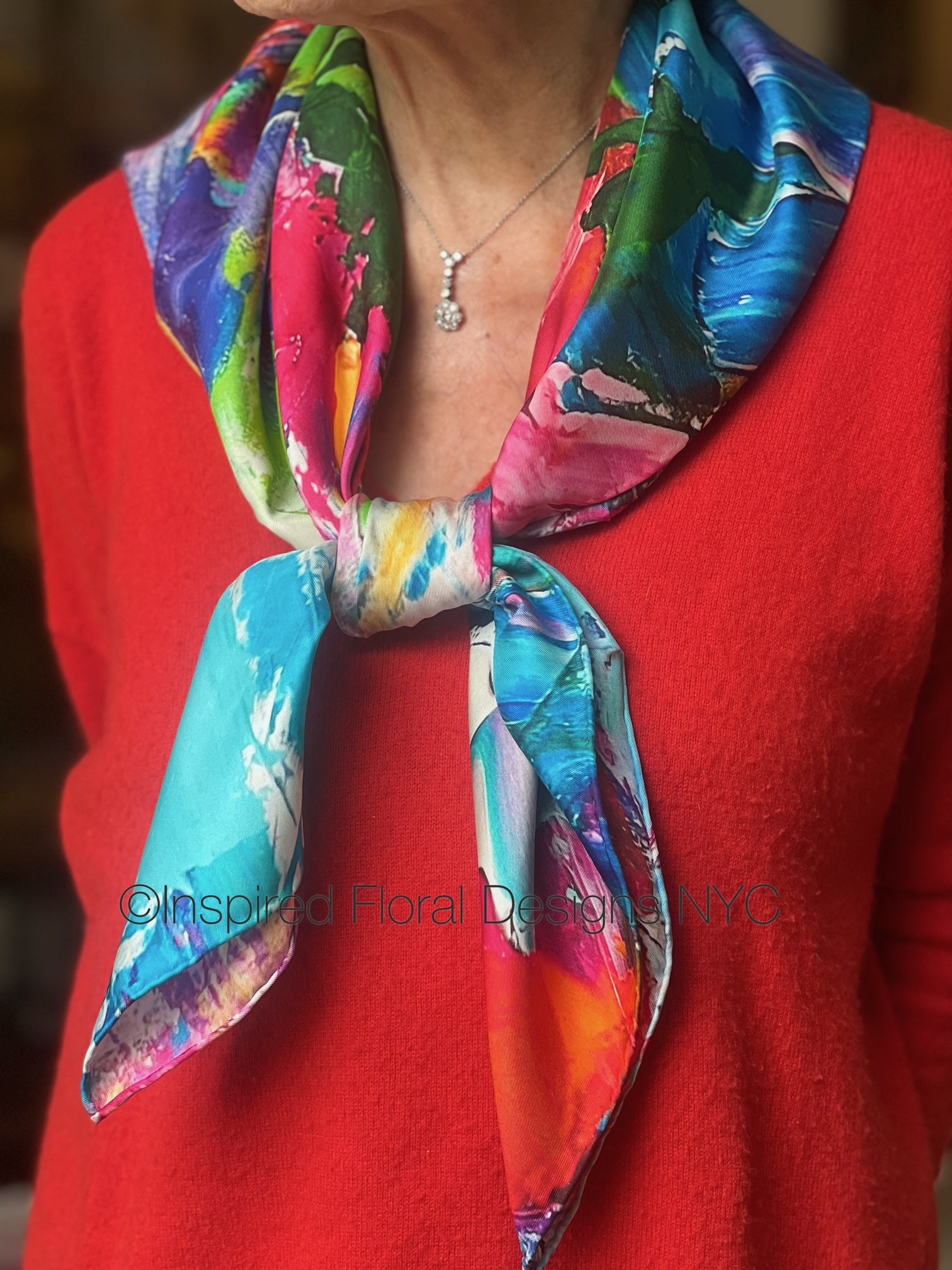 Person wearing a colorful floral abstract scarf titled petals unleashed by inspired floral designs nyc on a red background copyright