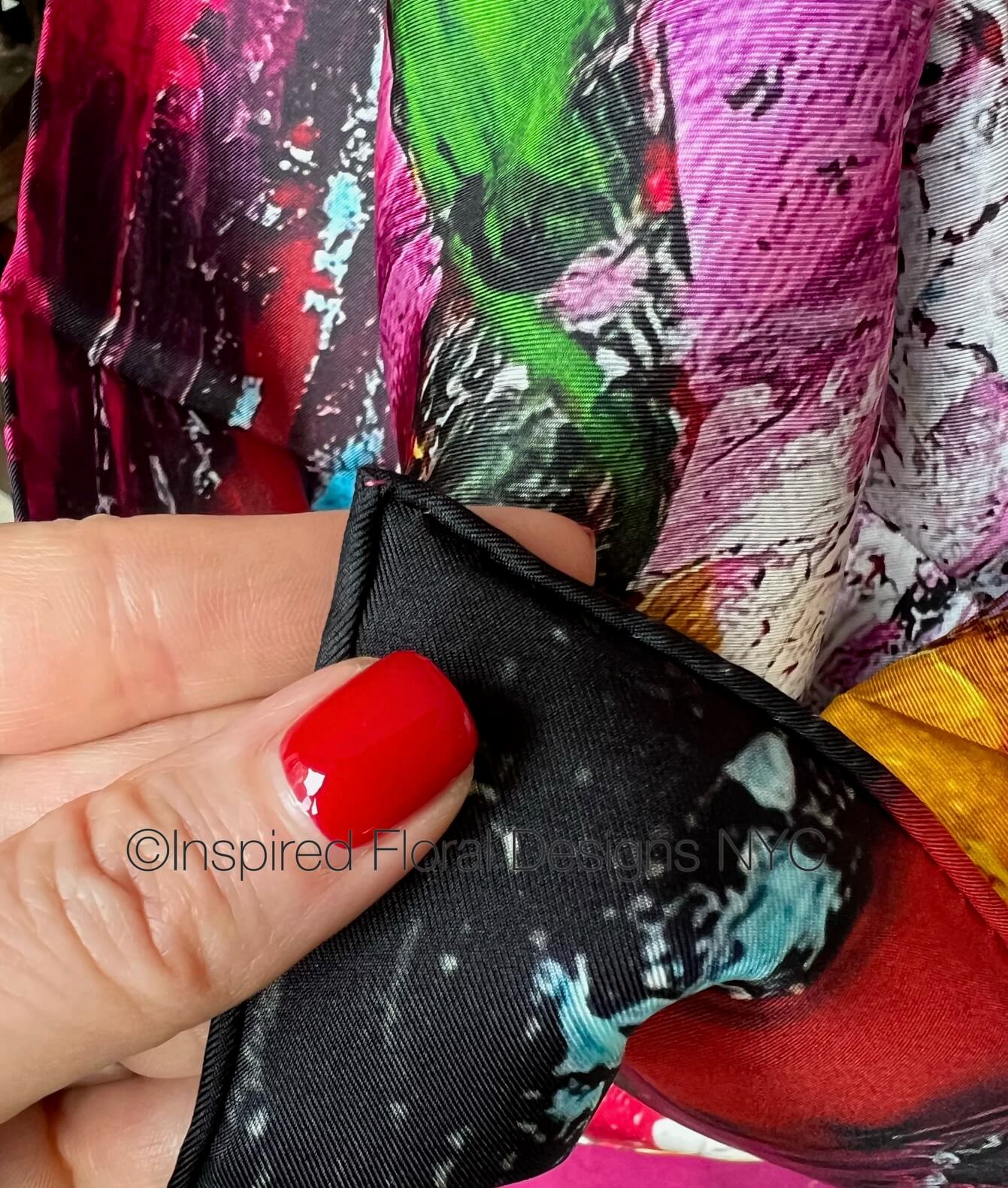 Close-up of a hand holding a colorful scarf petals in the wild by inspired floral designs nyc with brand name visible. copyright 