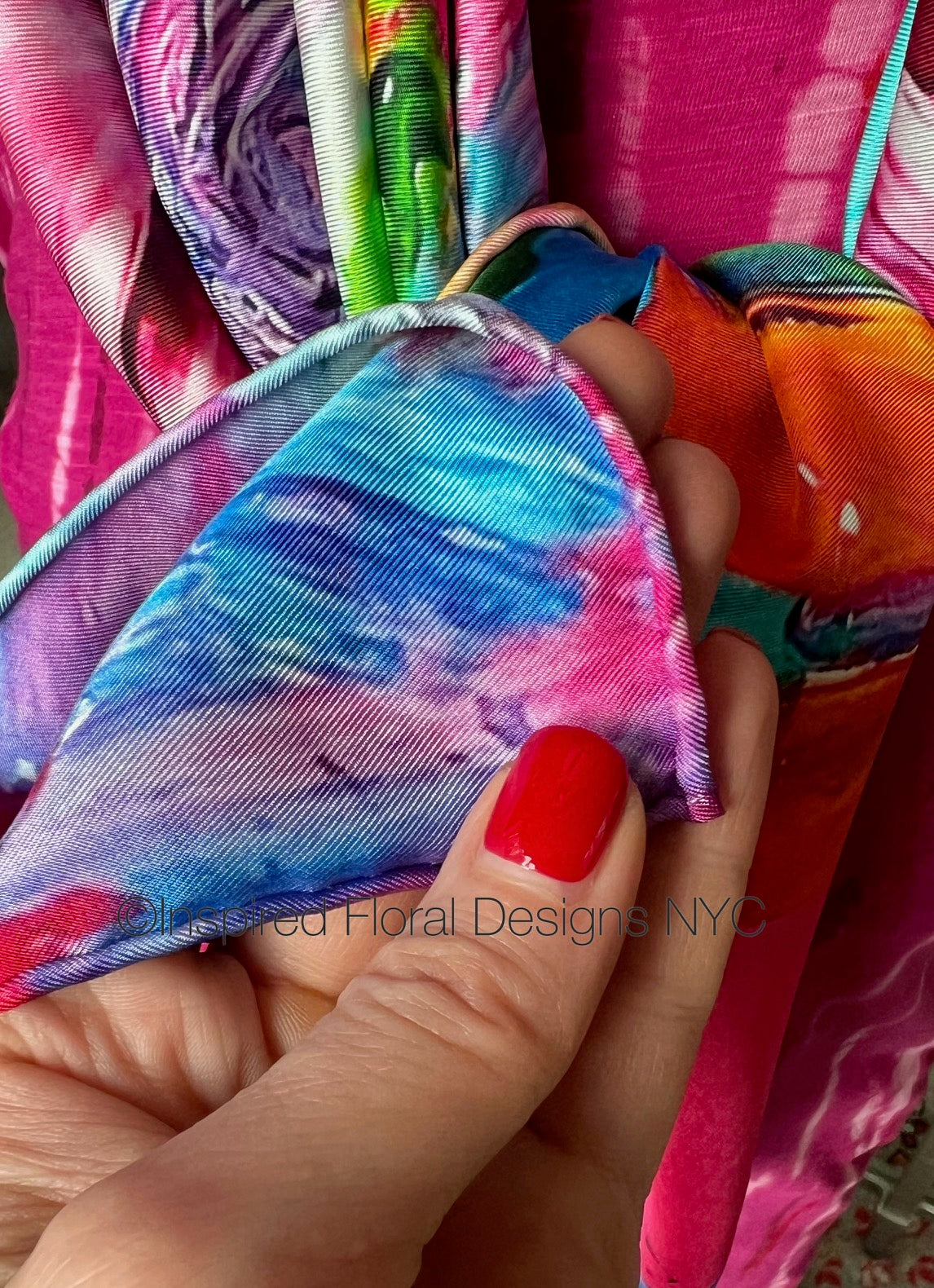 Colorful fabric with floral designs titled petals unleashed by inspired floral designs nyc held by a hand with red nail polish. copyright