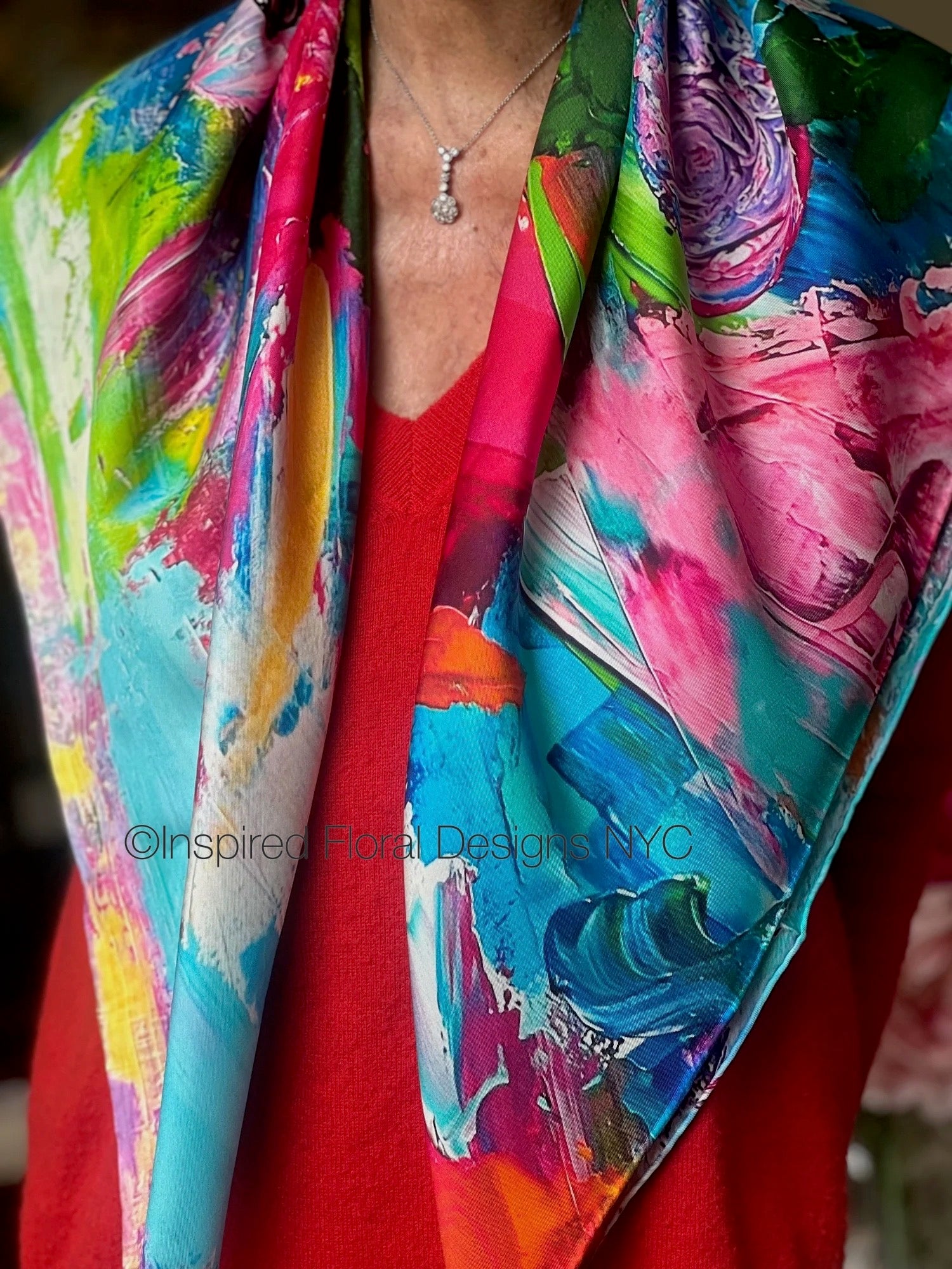 Colorful abstract floral patterned scarf draped over a person wearing a red garment copyright inspired floral designs nyc titled petals unleashed