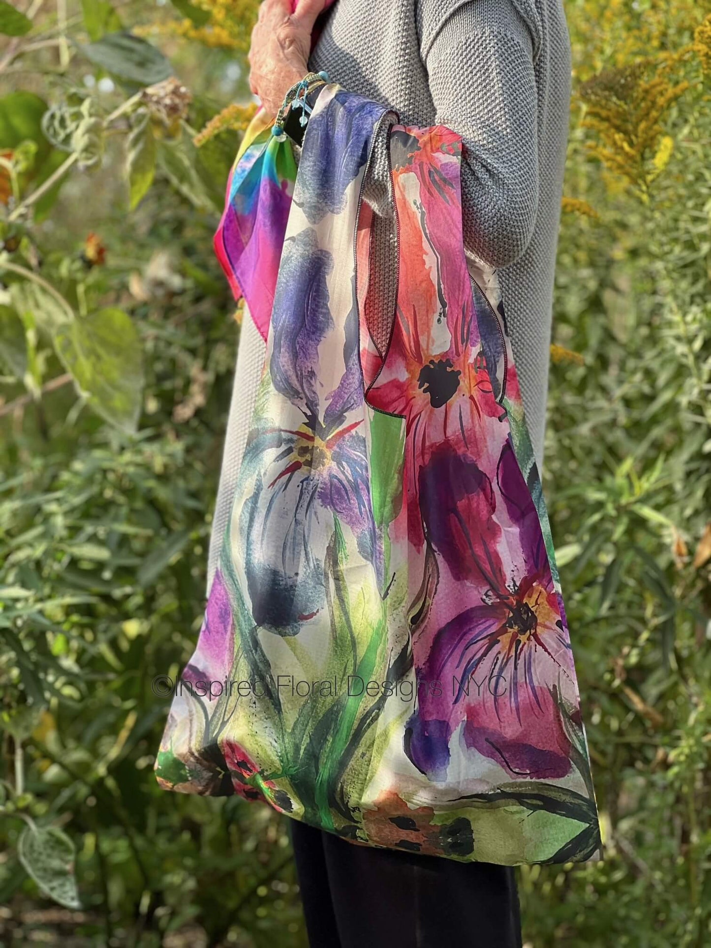 Person holding a colorful tote bag with floral design against a natural background by inspired floral designs nyc copyright