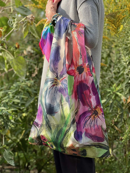 Person holding a colorful tote bag with floral design against a natural background by inspired floral designs nyc copyright