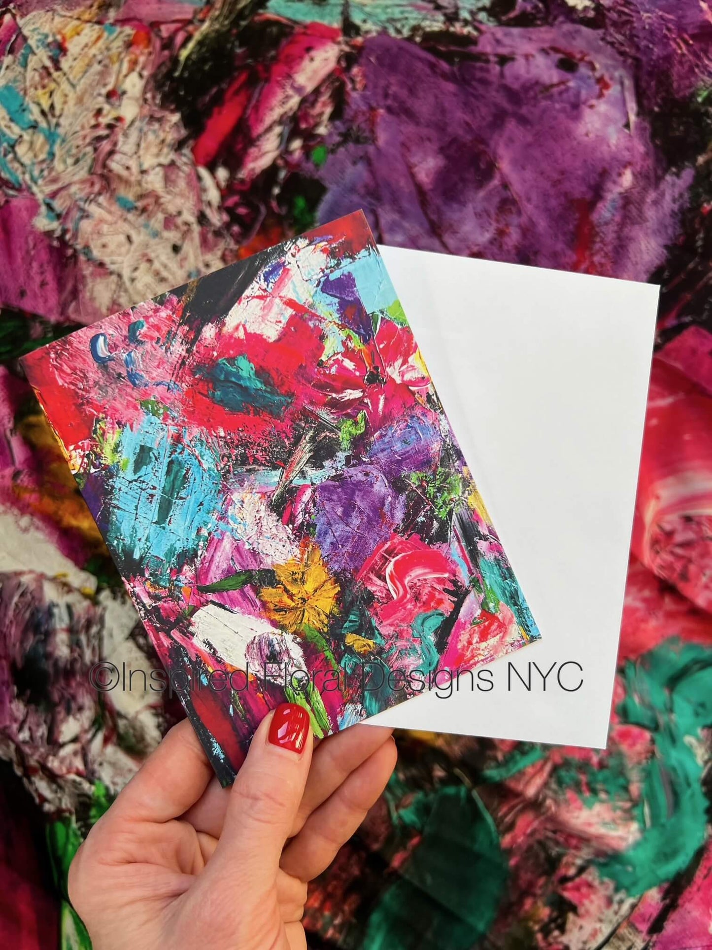 Colorful abstract art card held by a hand with a white card displaying Inspired Floral Designs NYC on a textured background copyright