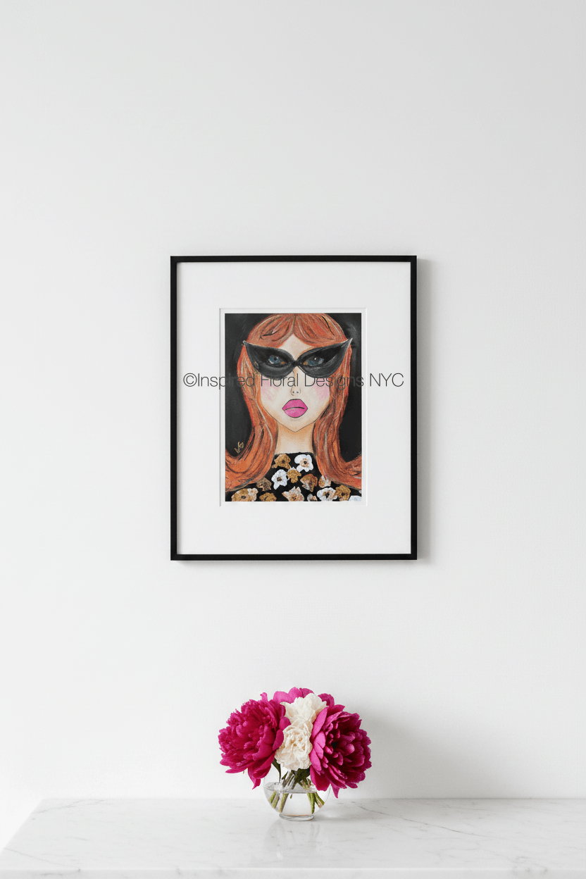 Framed artwork of a woman's face with sunglasses on a white wall, accompanied by a small vase with flowers by Inspired Floral Designs NYC LLC Copyright