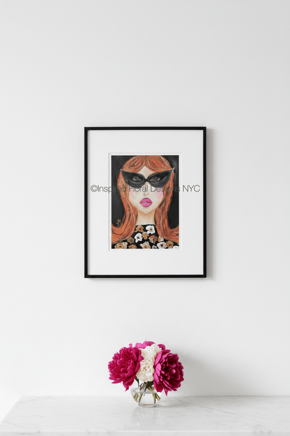 Framed artwork of a woman's face with sunglasses on a white wall, accompanied by a small vase with flowers by Inspired Floral Designs NYC LLC Copyright