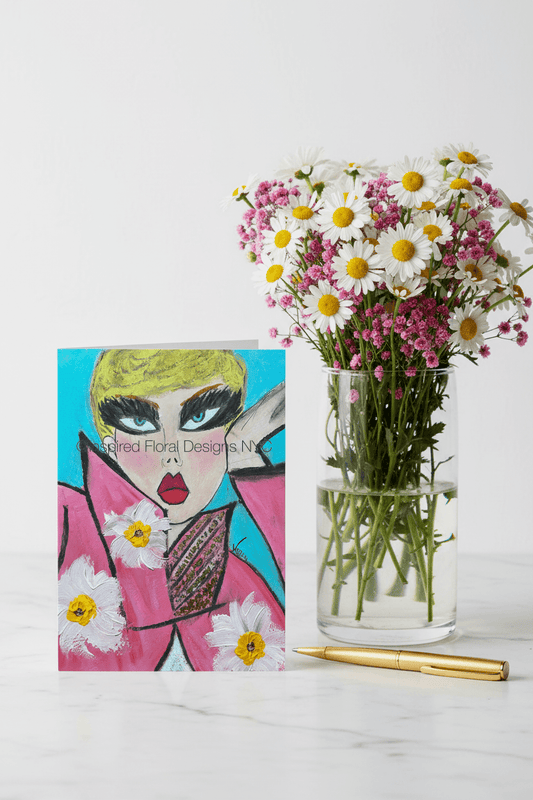 Vase with flowers next to a colorful card with a face design on a white surface by inspired floral designs nyc llc copyright