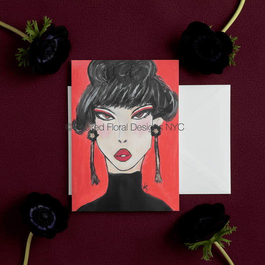 A square greeting card featuring a stylized illustration of a woman with black hair, red lips, and a red background, shown with a white envelope on a dark burgundy surface surrounded by black flowers by Whitney at Inspired Floral Designs NYC LLC. A watermark reading 'Inspired Floral Design NYC' is visible across the center copyright. 