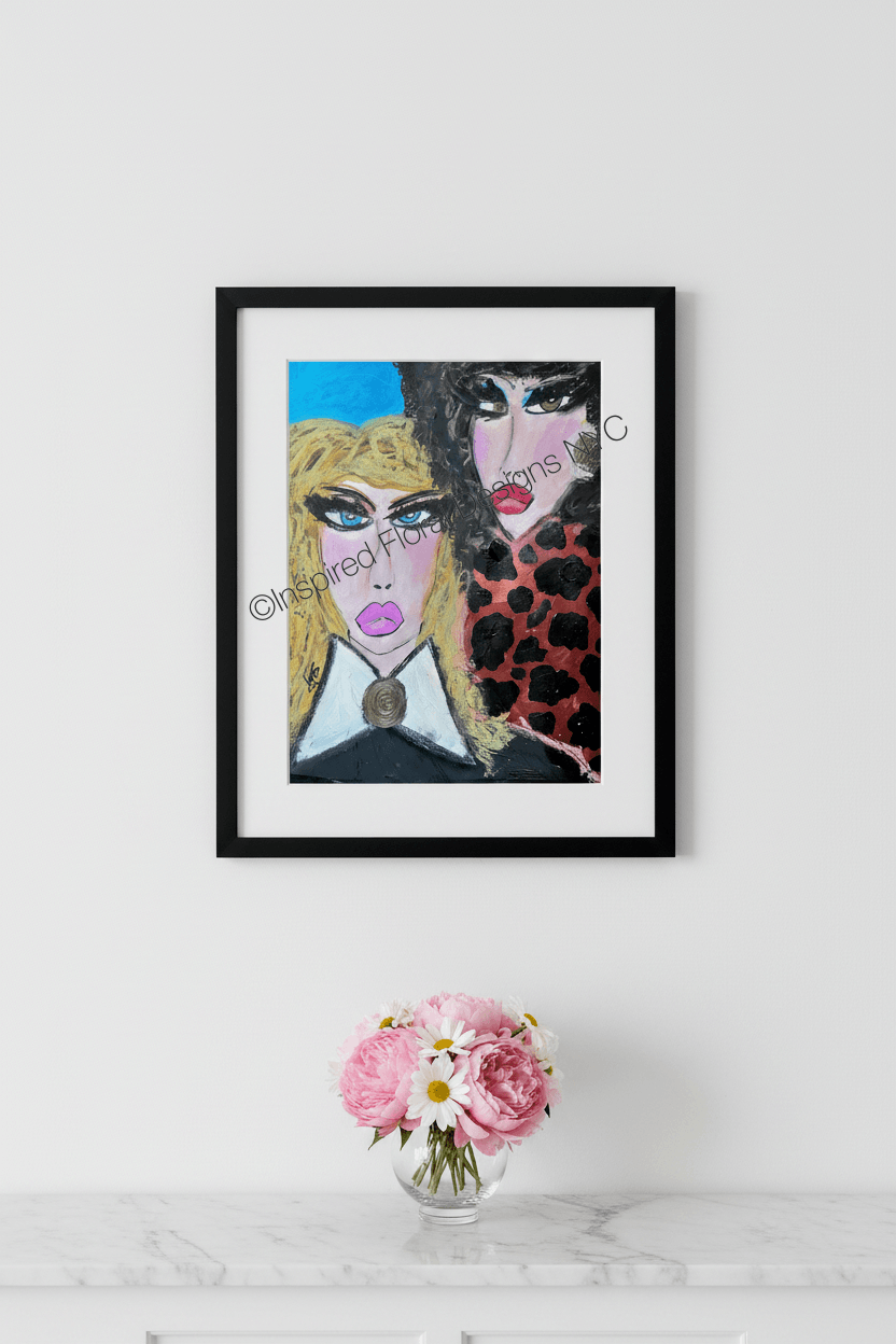 A framed art print featuring a stylized portrait of two women with bold colors, displayed on a white wall above a marble surface with a small vase of pink flowers by Whitney at Inspired Floral Designs NYC LLC copyright