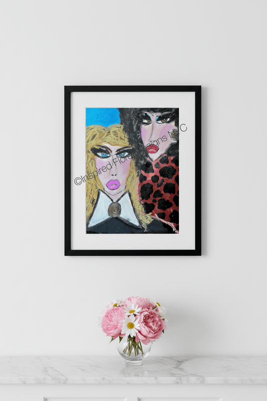 A framed art print featuring a stylized portrait of two women with bold colors, displayed on a white wall above a marble surface with a small vase of pink flowers by Whitney at Inspired Floral Designs NYC LLC copyright