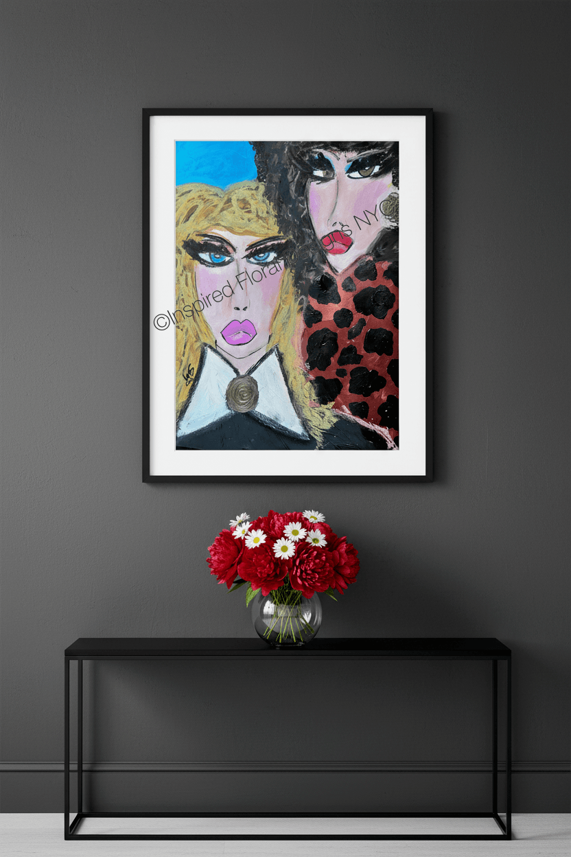 A framed art print featuring a stylized portrait of two women, displayed on a dark gray wall above a black console table with a red and white flower arrangement by Whitney at Inspired Floral Designs NYC LLC copyright