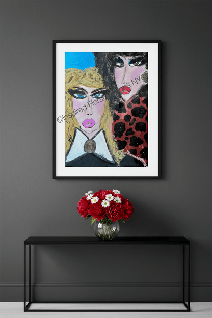 A framed art print featuring a stylized portrait of two women, displayed on a dark gray wall above a black console table with a red and white flower arrangement by Whitney at Inspired Floral Designs NYC LLC copyright