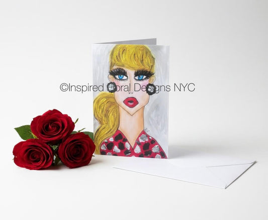 A vertical greeting card featuring a stylized illustration of a woman with blonde hair, blue eyes, and red lips, shown standing upright next to three red roses and a white envelope on a light gray background by Whitney at Inspired Floral Designs NYC LLC. A watermark reading 'Inspired Floral Designs NYC' is overlaid across the center.