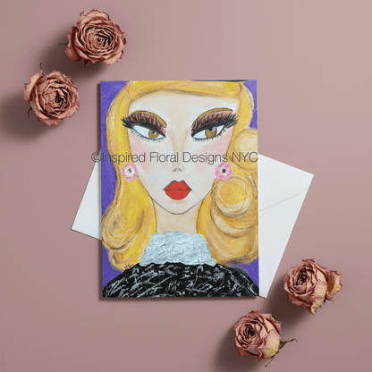 A greeting card featuring a stylized illustration of a blonde woman with bold makeup and red lips, shown with a white envelope on a dusty pink background with dried pink roses around it by Whitney at Inspired Floral Designs NYC LLC.  A watermark reading 'Inspired Floral Designs NYC' is visible across the artwork copyright.