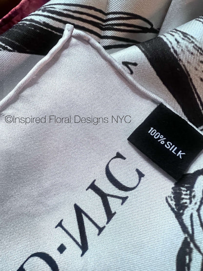 Close-up of a white silk scarf with black graphic print and a black fabric tag reading '100% SILK' and inspired floral designs nyc copyright 