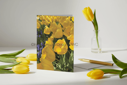 Greeting card with yellow tulips design on a white surface with additional tulips and a pen by Inspired Floral Designs NYC LLC