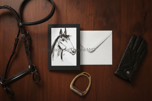 Horse bridle, framed drawing of a horse head by Whitney, envelope, and black glove on a wooden surface. Inspired Floral Designs NYC LLC copyright