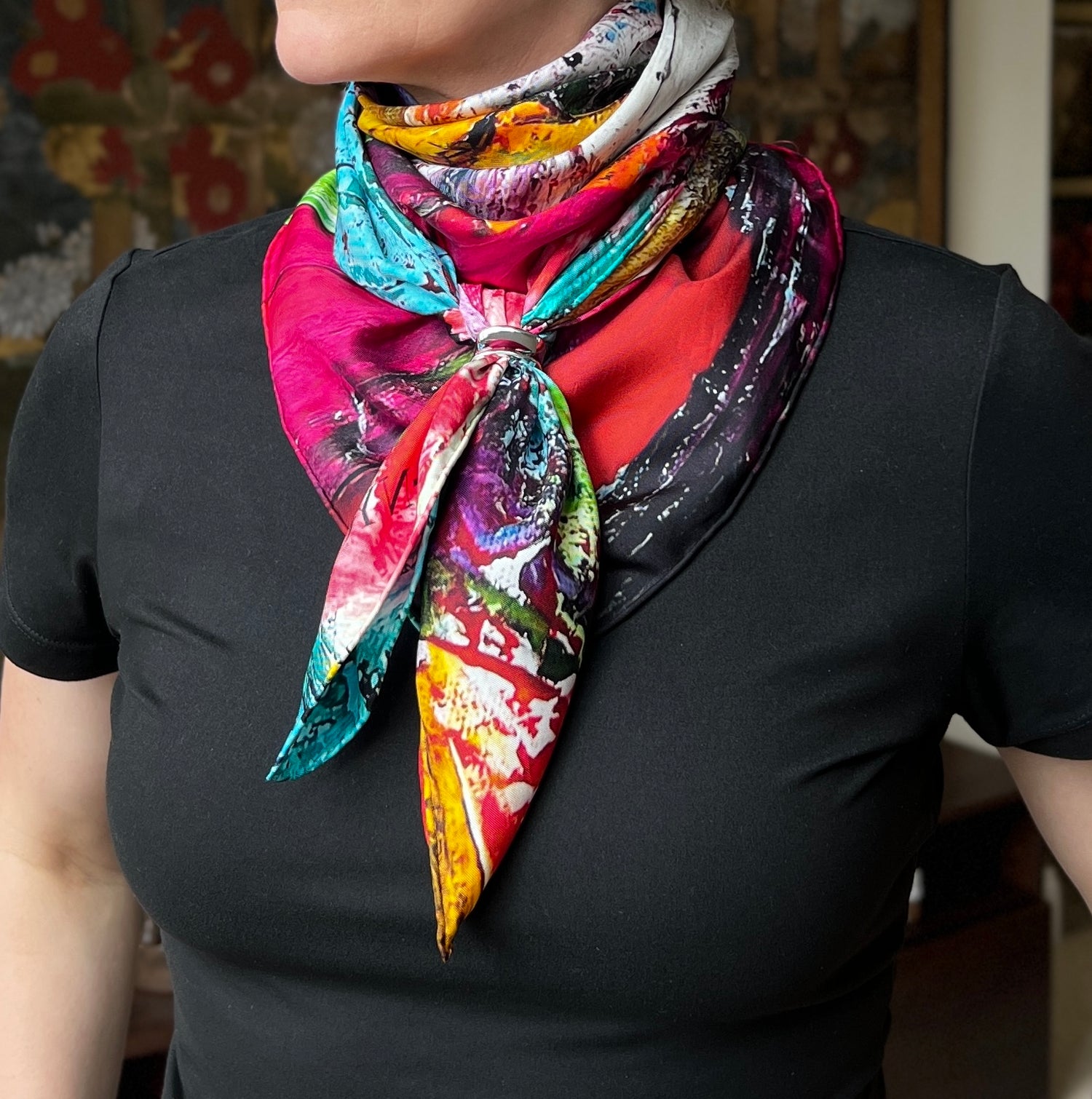 Person wearing a colorful abstract floral silk twill scarf on a black shirt with a blurred background- scarf is petals in the wild by inspired floral designs nyc