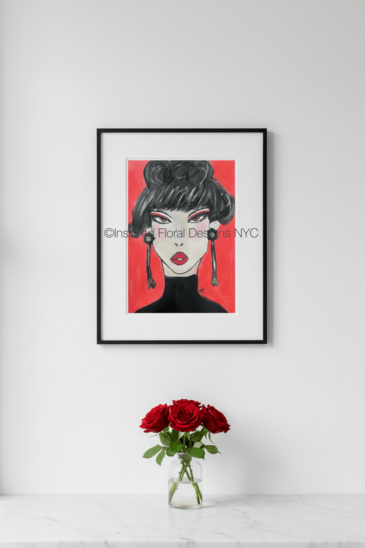 Framed artwork of a stylized face with red background on a white wall, next to a vase of red roses by Inspired Floral Designs NYC LLC copyright