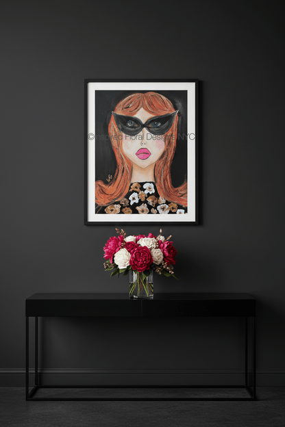 Framed artwork of a woman's face with red hair and black mask on a dark wall above a black console table with flowers by Inspired Floral Designs NYC LLC copyright