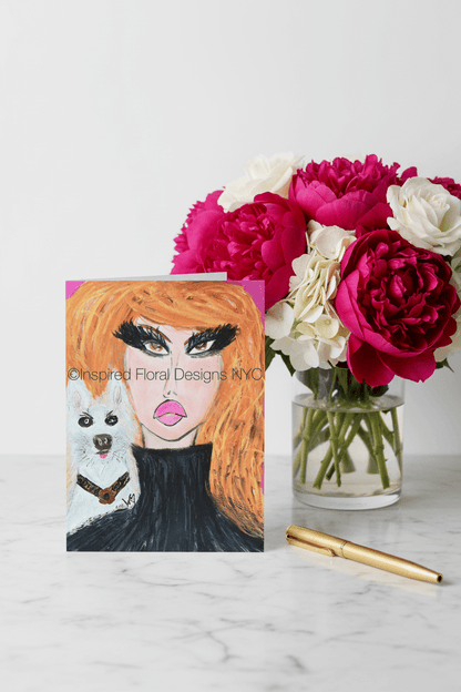 Card with a face design and dog illustration next to a vase of flowers on a marble surface by inspired floral designs nyc llc copyright
